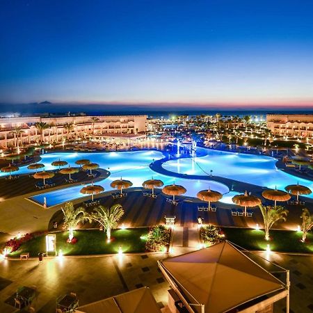 منتجع رويال الباتروس مودرنا - للعائلات والأزواج فقط شرم الشيخ المظهر الخارجي الصورة The photo showcases an elegant resort area at dusk. It features a large swimming pool, which is beautifully illuminated with blue lights, creating a serene and inviting atmosphere. Surrounding the pool are palm trees and umbrellas, enhancing the trop
