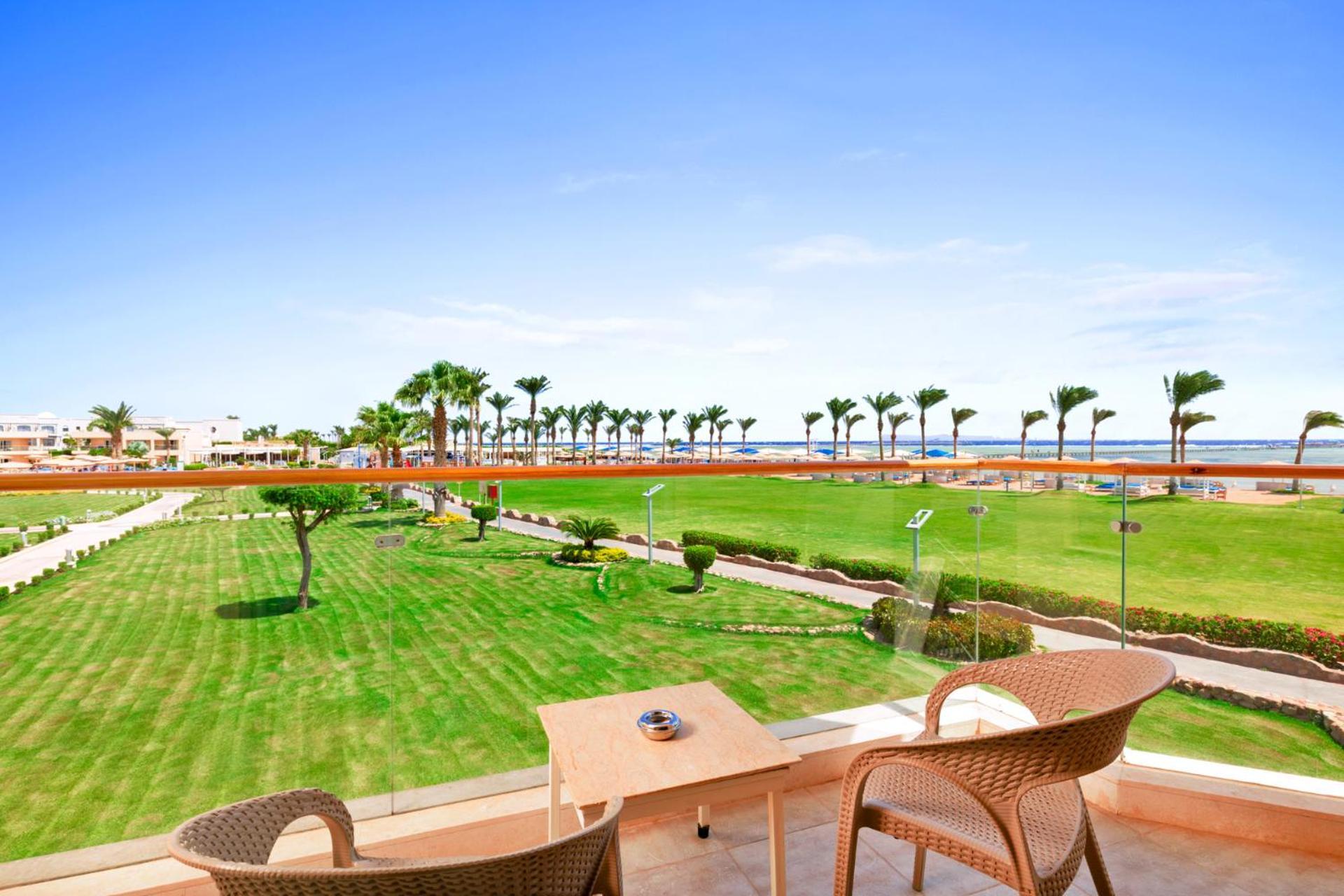 منتجع رويال الباتروس مودرنا - للعائلات والأزواج فقط شرم الشيخ المظهر الخارجي الصورة The photo shows a scenic view from a balcony overlooking a lush green lawn. There are two outdoor chairs and a small table on the balcony. In the background, palm trees line the pathway leading to the beach, which is visible in the distance under a c