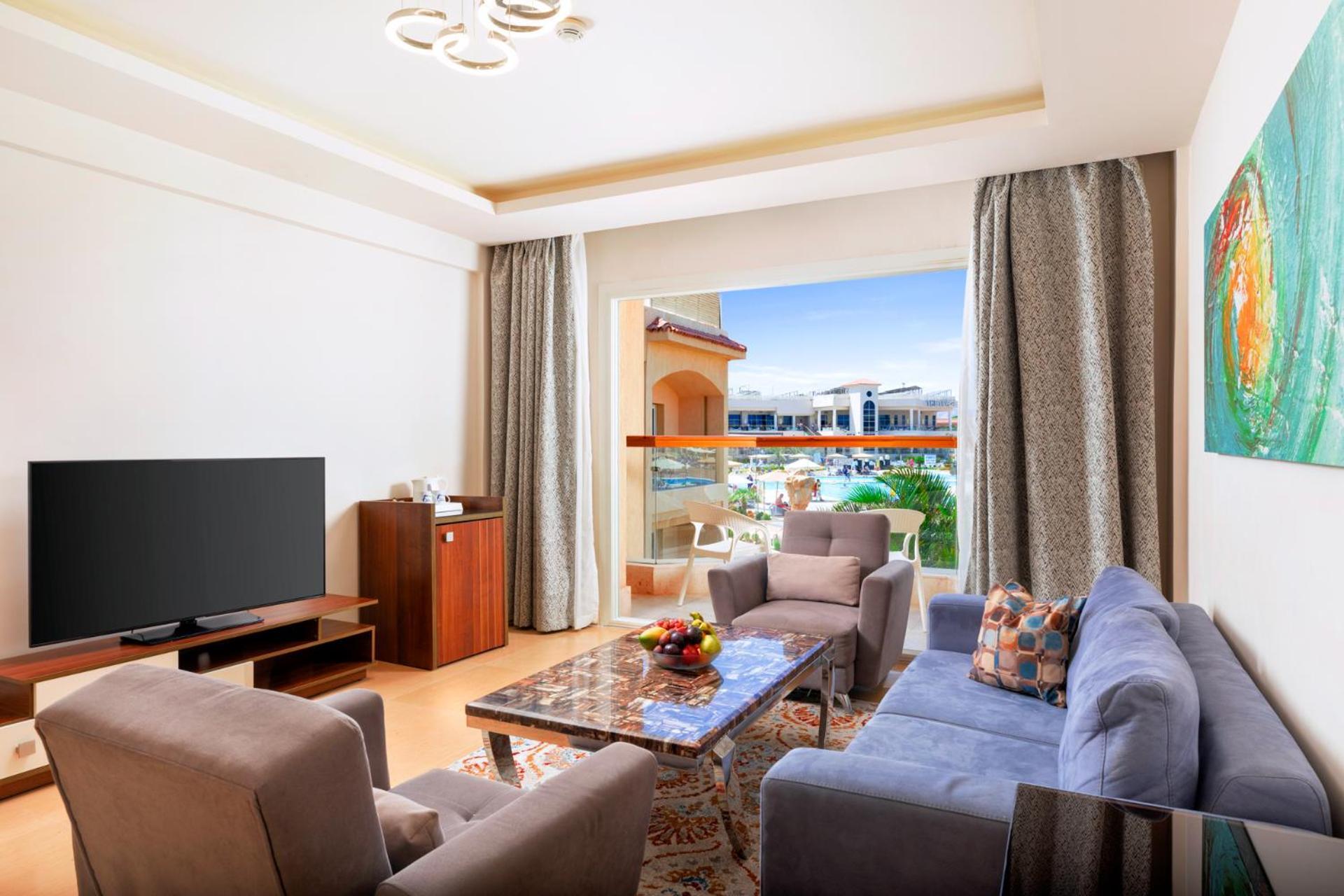 منتجع رويال الباتروس مودرنا - للعائلات والأزواج فقط شرم الشيخ المظهر الخارجي الصورة The photo shows a modern and stylish living room. It features a comfortable seating arrangement with a gray sofa and two armchairs, a coffee table in the center, and a wooden TV stand with a large flat-screen TV. There are large windows with curtains