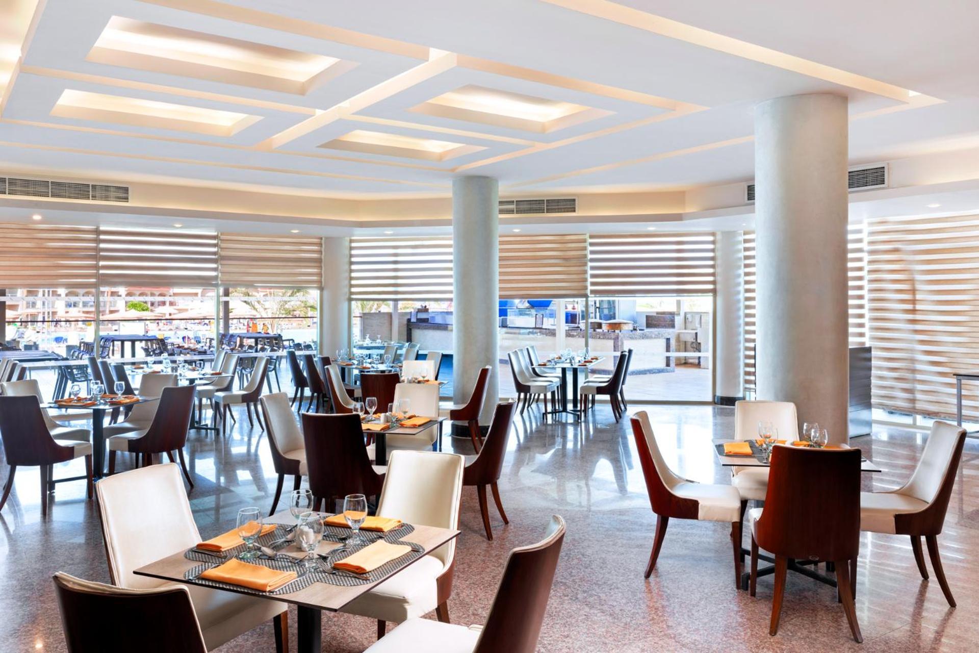منتجع رويال الباتروس مودرنا - للعائلات والأزواج فقط شرم الشيخ المظهر الخارجي الصورة The photo shows a modern restaurant interior. It features a spacious dining area with a combination of brown and white chairs arranged around tables. The design includes elegant, contemporary decor with soft lighting and a ceiling with geometric patt