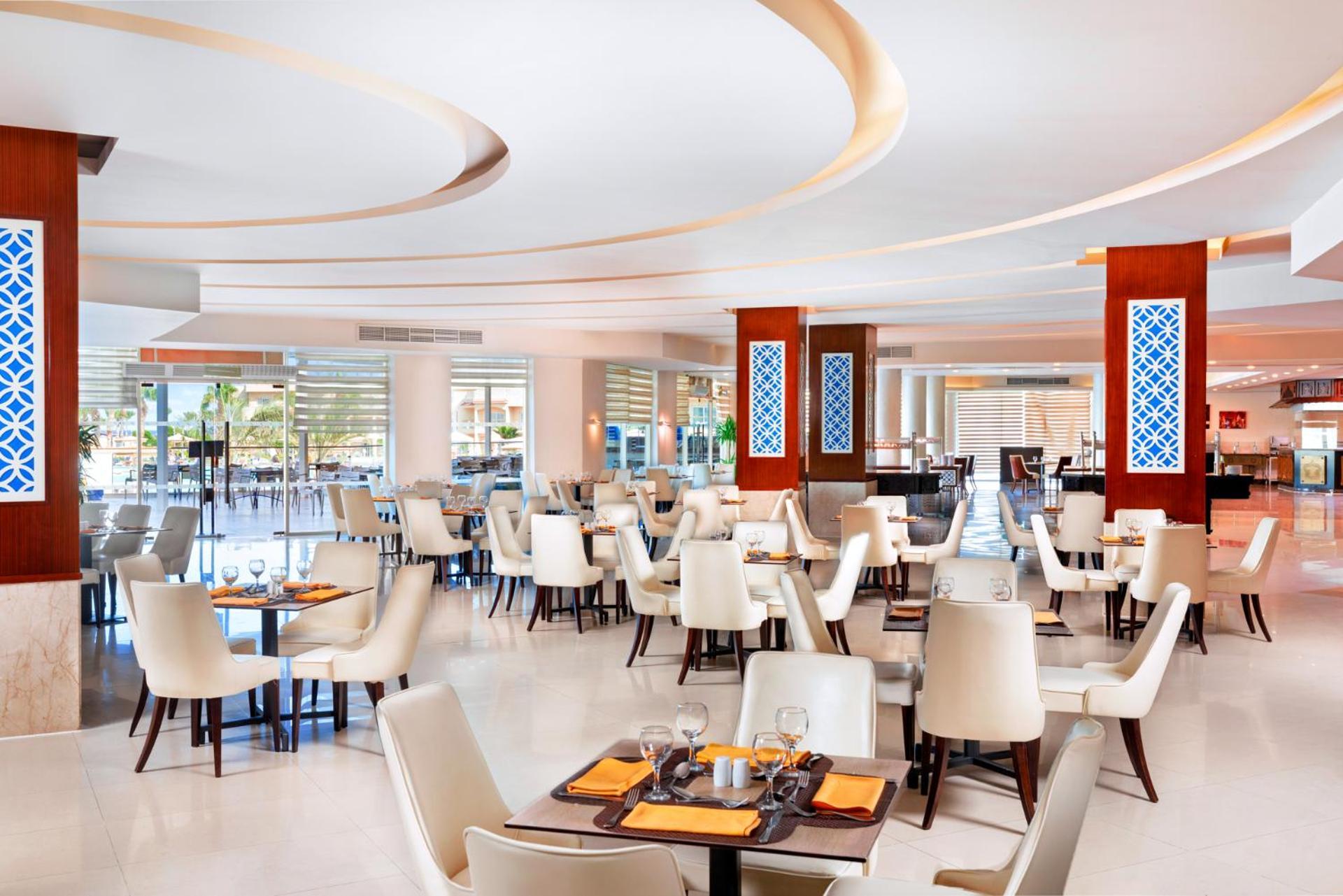 منتجع رويال الباتروس مودرنا - للعائلات والأزواج فقط شرم الشيخ المظهر الخارجي الصورة The photo shows a modern restaurant interior. The design features light, neutral colors with elegant white chairs and wooden tables. The layout includes several dining tables set for customers, creating a spacious and inviting atmosphere. There are d
