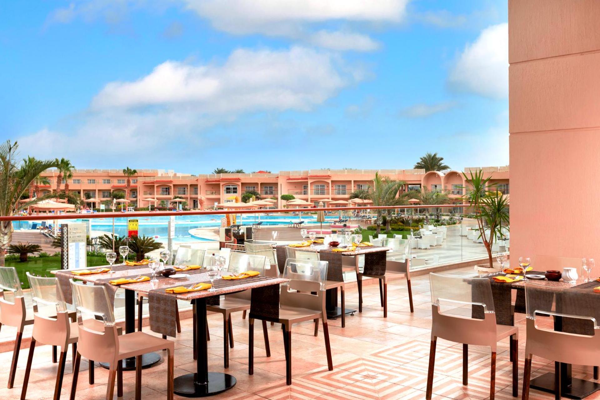 منتجع رويال الباتروس مودرنا - للعائلات والأزواج فقط شرم الشيخ المظهر الخارجي الصورة The photo shows an outdoor dining area at a resort. There are several tables set for dining, featuring elegant tableware. In the background, a large swimming pool is visible, surrounded by lush greenery and lounge chairs. The buildings beyond the poo