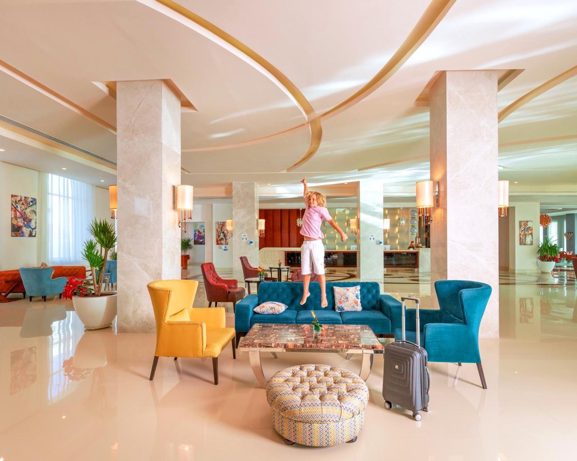 منتجع رويال الباتروس مودرنا - للعائلات والأزواج فقط شرم الشيخ المظهر الخارجي الصورة The photo shows a modern and stylish hotel lobby. There's a spacious area with elegant decor, featuring large pillars and contemporary lighting. A colorful arrangement of furniture includes teal, yellow, and red chairs. A person is standing on a larg